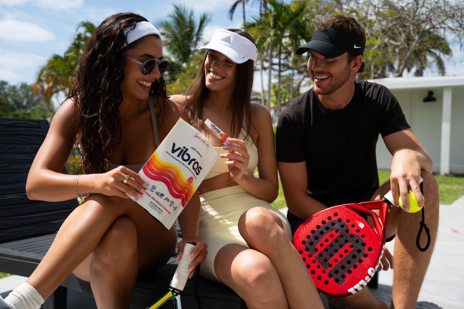 Two females and one male padel player hold rackets, balls and the padel supplement called Vibras