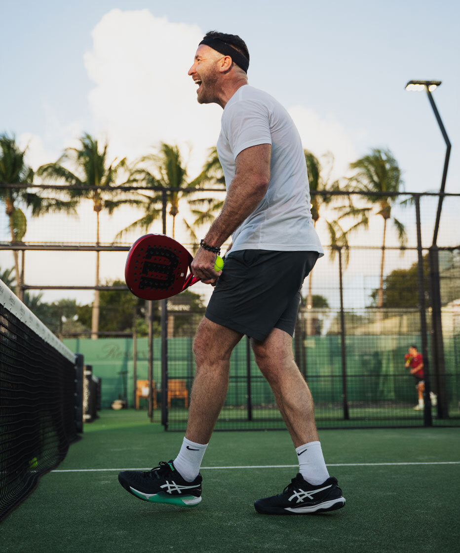 Man playing padel on a court with palm trees in the background