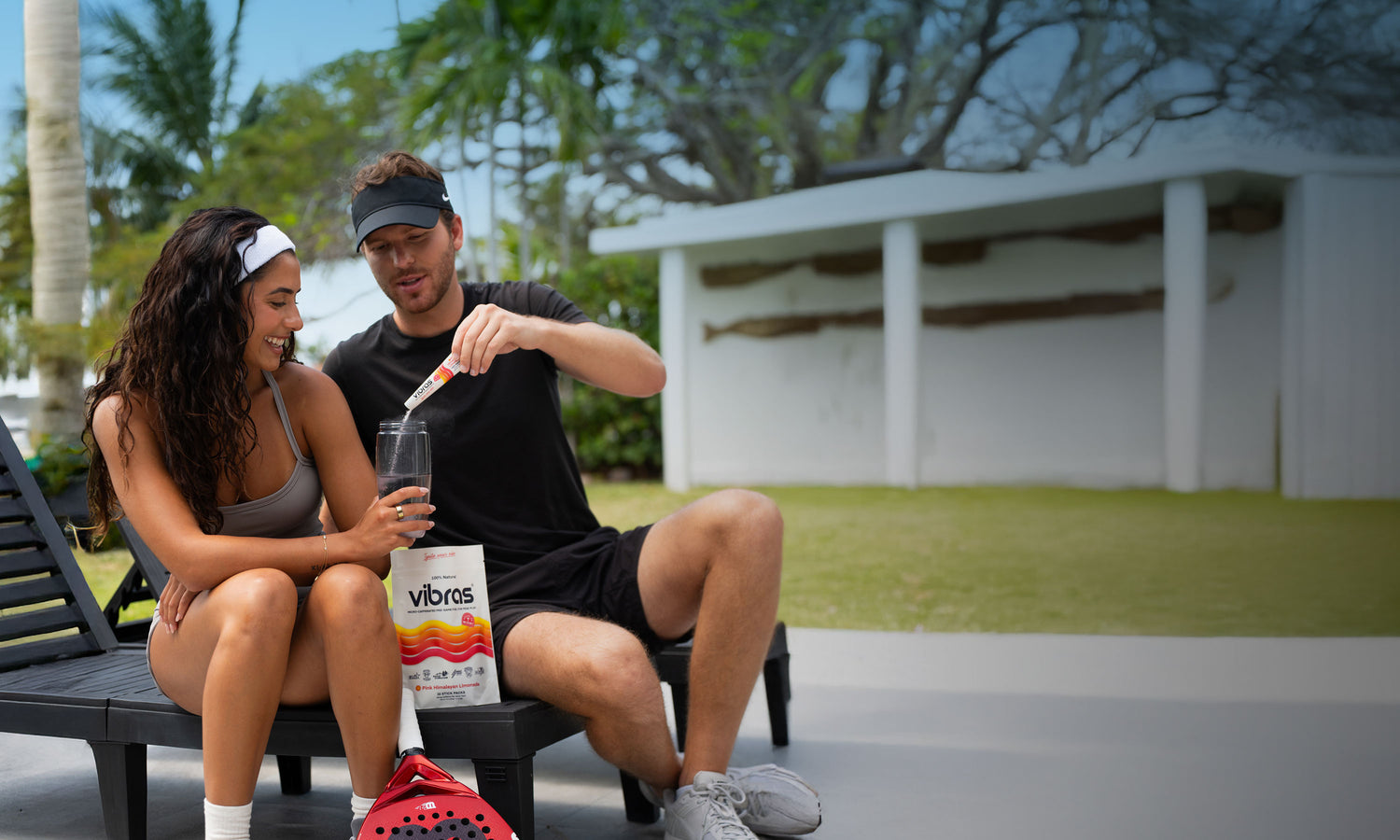 A man pours a stick pack of Vibras into a girls sports bottle with padel equipment around them
