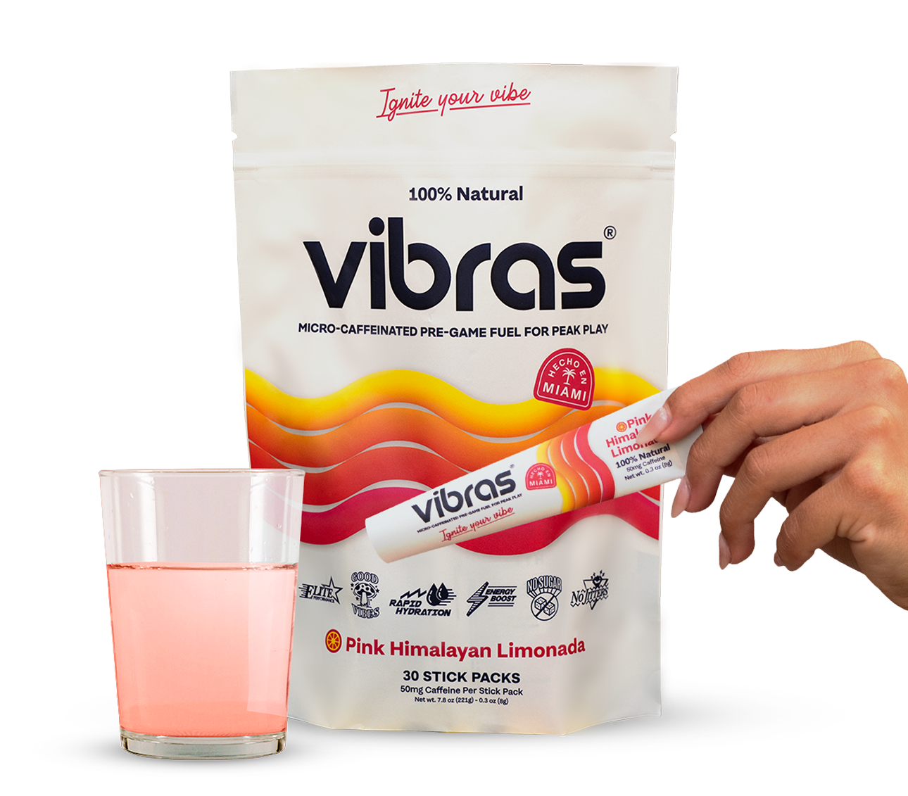 A hand holding a Vibras stick pack next to a Vibras pouch and a cup with pink lemonade in it